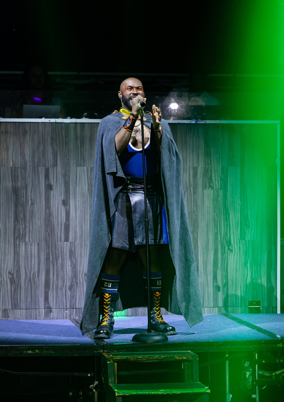 Jace The Caveat performing in a leather kilt and cape under green stage light