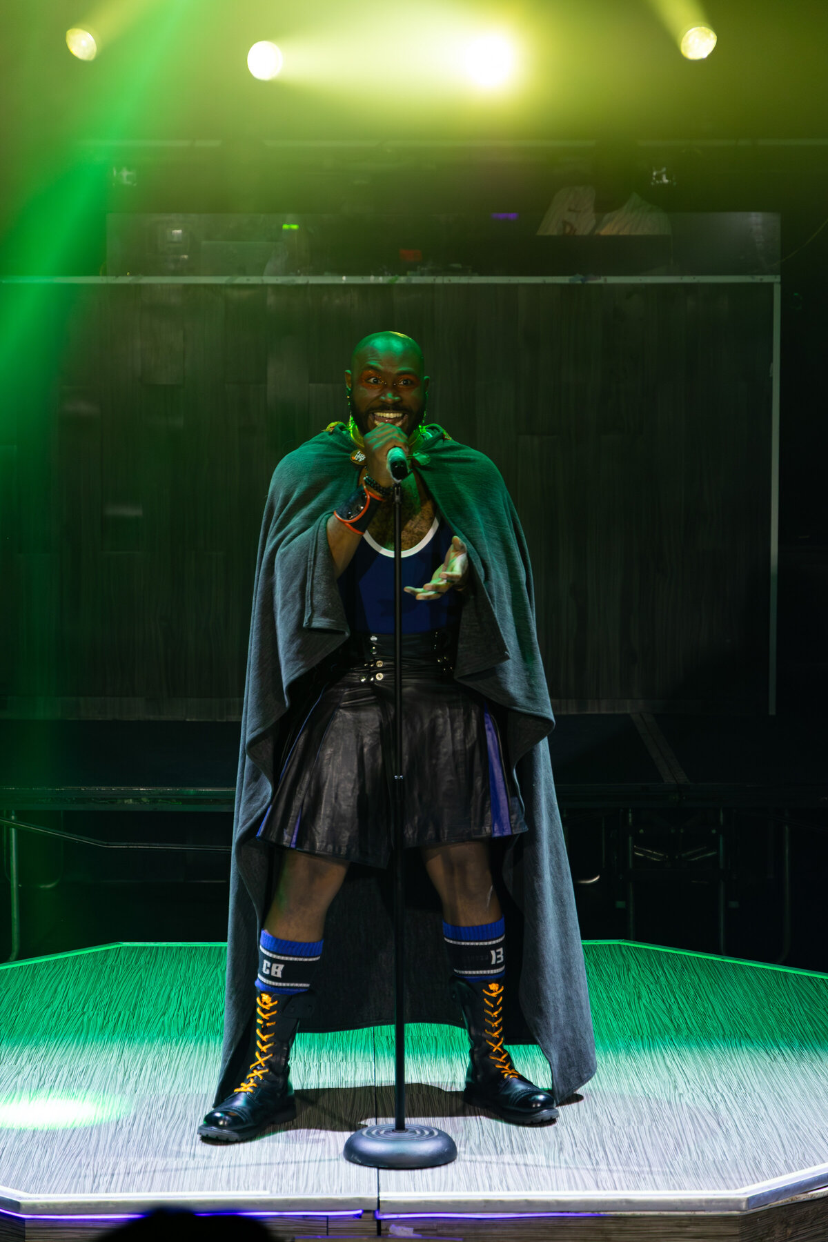 Jace The Caveat singing into a mic stand, full length, green wash
